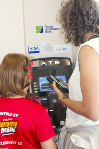 A young  bank customer is helped at the ATM by her mom.