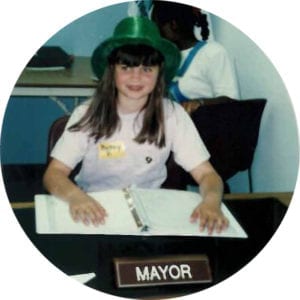 Mayor Betsy Poell smiles in a green hat. She is the mayor of Young AmeriTowne