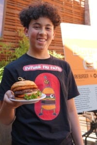 Cameron at Burger Biz smiles while holder their burger creation