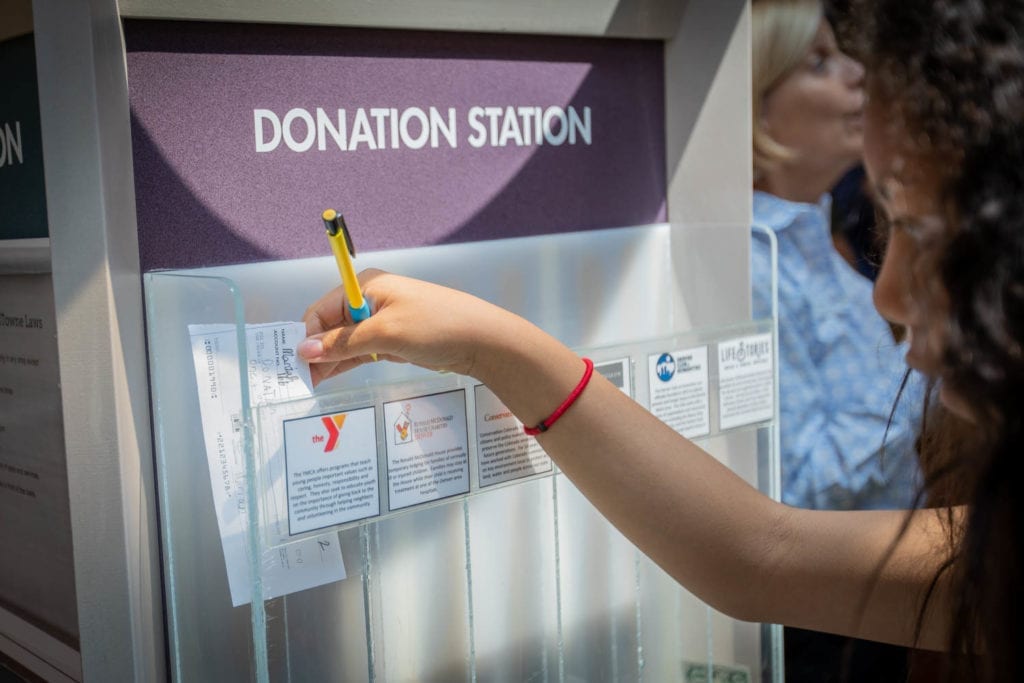 Girl puts cash in Young AmeriTowne donation bin
