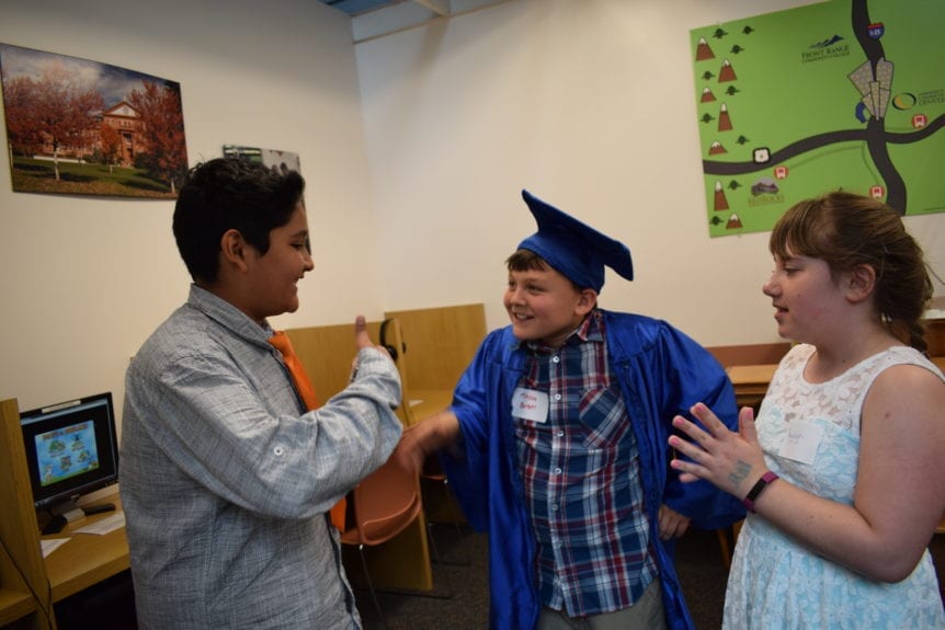 Students Shake Hands in the AmeriTowne College with graduation cap and outfit. Two other students handshake and praise the graduate.