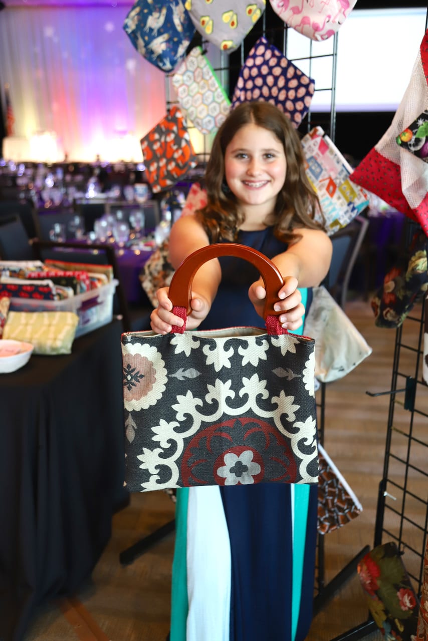 Maile McManis, 2020 YouthBiz Star finalist holding a fabric handbag with wooden handles