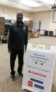 State Farm Volunteer Lawrence Neal standing next to a sign for Young AmeriTowne on the Road