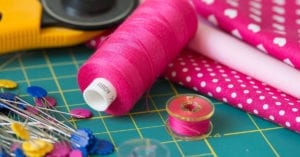 Sewing Supplies Iconography with a spool of pink thread, straight pins, and various pink fabrics